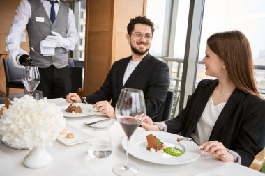 Gülümseyen genç çift restoranda birbirlerine bakarken garsonlar şarap dolduruyor. Romantizm, tarih, ilişki kavramı