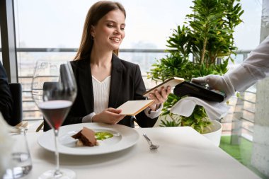 Kahvede NFC teknolojisini kullanarak faturaları ödeyen gülümseyen genç bir kadın. Teknoloji konsepti