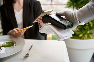 Lokantada NFC teknolojisiyle faturasını ödeyen genç bir kadın. Teknoloji konsepti