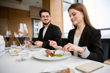 Gülümseyen genç adam ve kadın modern restoranda oturmuş yemeğin tadını çıkarıyorlar. Romantizm, tarih, ilişki kavramı