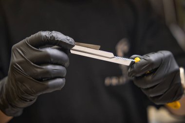 Koruyucu siyah eldivenli yakın plan berber elinde jilet, müşterileri ipeksi, pürüzsüz bırakarak müşterilerle çalışmak için profesyonel aletler hazırlıyor.