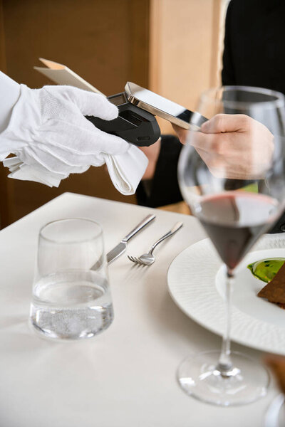 Vertical photo of male customer paying bill through phone using NFC technology in restaurant. Technology concept