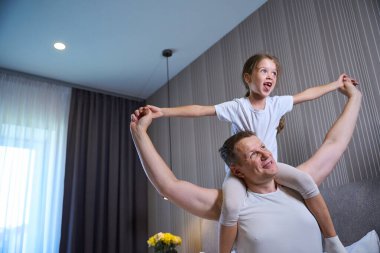Baba ve küçük kızı eğlenceli bir sabah uyanıyor, kız babasının omuzlarında oturuyor.