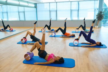 Antrenman odasında spor yapan bir grup kadın silindirler üzerinde egzersiz yapıyor.