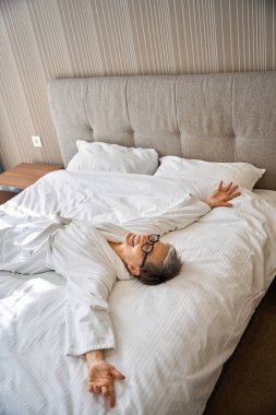 Otel odasında rahat bir yatakta yatarken bornozlu, mutlu beyaz kadın dinleniyor. Seyahat, insanlar, yaşam tarzı konsepti