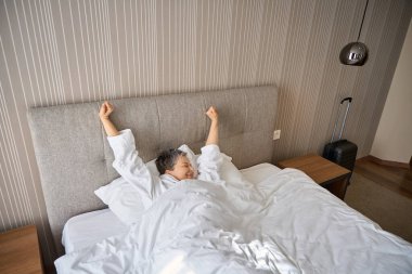Beyaz bornozlu güzel yetişkin kadın yatakta dinleniyor, otel odasında sabahın tadını çıkarıyor. Seyahat, insanlar, yaşam tarzı konsepti