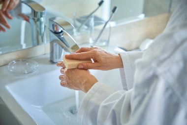 Bornozlu bir kadının banyoda sabunla ellerini yıkarken çekilmiş fotoğrafı. Seyahat, insanlar, yaşam tarzı konsepti