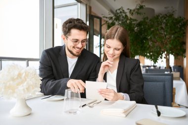 Gülümseyen genç adam ve kadın restoranda oturmuş menüden yemek seçiyorlar. Romantizm, tarih, ilişki kavramı