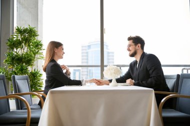 Gülümseyen romantik adam ve kadın restoranda el ele tutuşup birbirlerine bakıyorlar. Yan görüş. Romantizm, tarih, ilişki kavramı