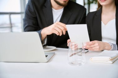 Restorandaki iş toplantısında dizüstü bilgisayarla masada oturan çift menüde bekliyor. İş, ortaklık, teknoloji kavramı
