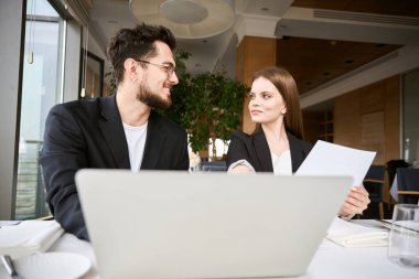 Laptopla çalışan gülümseyen iş ortakları ve restoranda birbirini arayan belgeler. İş, ortaklık, teknoloji kavramı