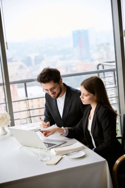Restoranda oturan genç adam ve kadın toplantı sırasında dizüstü bilgisayarla çalışıp notlar alıyorlar. İş, ortaklık, teknoloji kavramı