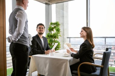 Lokantada sipariş veren ve garsona bakan mutlu genç adam ve kadın. Romantizm, tarih, ilişki kavramı