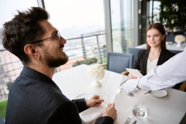 Mutlu sakallı bir adam restoranda kız arkadaşıyla oturmuş menüyü tutuyor, garsona bakıyor. Romantizm, tarih, ilişki kavramı