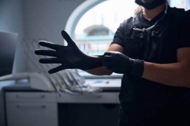 Doktor siyah koruyucu eldiven takıyor ve boynunda dürbün gözlüğü var.