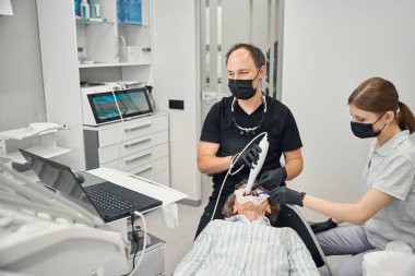 Uzman ve asistanı yaşlı bir bayanın dişlerini modern aletlerle tedavi ediyorlar.