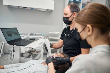 Doktor, genç bir asistanın yardımıyla yaşlı bir bayanın dişlerini yeniliyor.