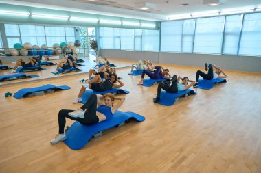 Kadınlar karın kaslarını güçlendirmek için egzersiz yaparlar, özel platformlar ve mavi paspaslar kullanırlar.