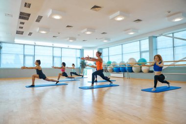 Kadınlar grubu rahat bir çalışma odasında iyi bir ruh hali içinde antrenman yapıyor. Odada büyük pencereler var.