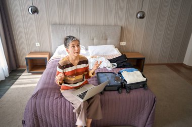Otel odasındaki yatakta dizüstü bilgisayarla çalışan gözlüklü yorgun iş kadını. Seyahat kavramı