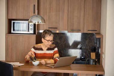 Çaydan hoşlanan olgun bir bayan ve oteldeki masada oturan dizüstü bilgisayarla çalışmak. Seyahat, iş konsepti