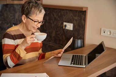 Çay içen, elinde dizüstü bilgisayarla otel odasında çalışan mutlu bir son sınıf öğrencisi. Seyahat, iş konsepti