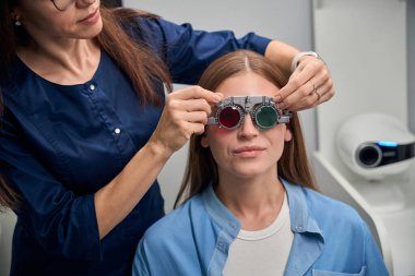 Yetişkin doktor hastaların yüzlerindeki deney lenslerini dikkatlice ayarlar ve görüş değerlendirmesine hazırlanır.