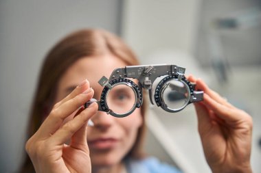 İki elinde bir deneme çerçevesi tutan genç bir kadın, bir optometri kliniğinde görme testi için hazırlanıyor.