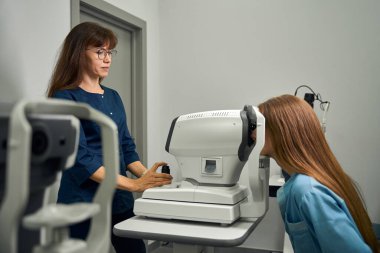Optometrist test sürecini izlerken genç bir kadın göz doktorunun önünde oturuyordu.