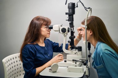 Yetişkin beyaz doktor ve hasta ileri seviye tanı ekipmanları kullanarak detaylı bir göz kontrolü sırasında etkileşime geçiyorlar.