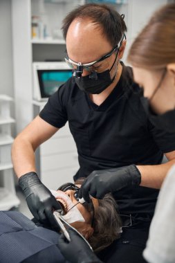 Cerrah ve asistanı yaşlı bir bayanın dişini sökmüş. Hasta dişçi koltuğunda oturuyor.