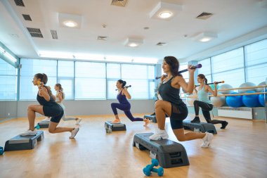 Keyifli kadınlar ayna önünde jimnastik sopalarıyla antrenman yapıyorlar, rahat spor ayakkabıları giyiyorlar.