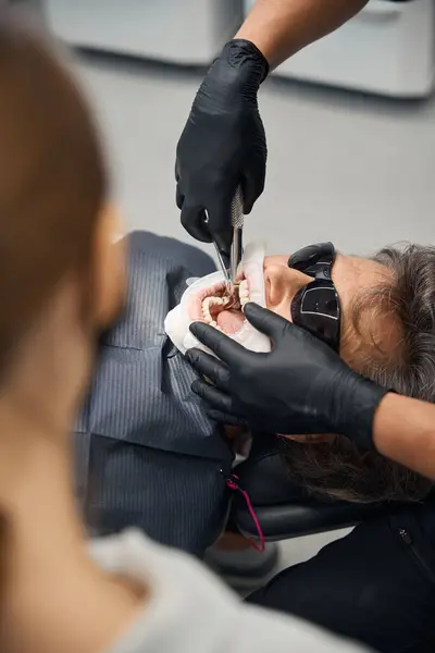 stock image Dental surgeon and an assistant remove a tooth from an elderly woman, the patient is seated in the dental chair