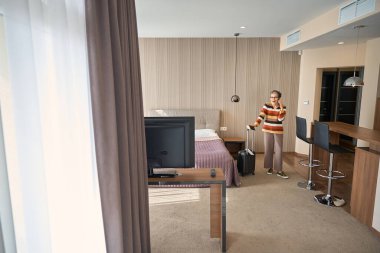 Bagajı olan gülümseyen yetişkin bir kadın, otel odasında telefonla konuşan seyahat belgeleri. Seyahat kavramı