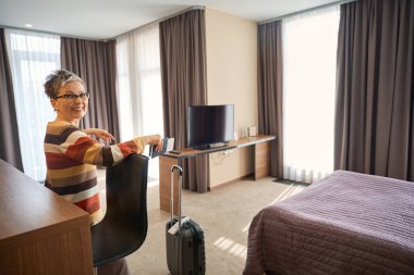Elinde biletlerle otel odasında kameraya bakarak gülümseyen yetişkin kadın. Seyahat kavramı
