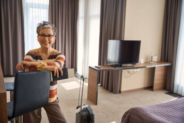 Çekici yetişkin kadın, elinde biletlerle otel odasında kameraya bakıyor. Seyahat kavramı