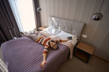 Otel odasındaki yatakta uzanan mutlu yaşlı bayanın manzarası. Seyahat kavramı