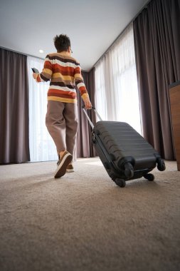 Biletli ve telefonlu yetişkin bir bayanın otel odasında bavuluyla dolaşması. Seyahat kavramı