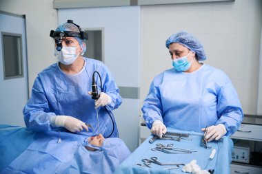 Steril ameliyathanede çalışan, modern teknolojileri kullanan, cerrahi giyimli insanlar.