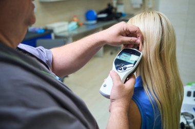 Doktor, klinikteki hastaların kulaklarını yakından incelemek için el bilgisayarı kullanıyor.