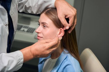 Kafkasyalı doktor, uygun bir seans sırasında genç bir kadın hastanın kulağına işitme cihazı yerleştiriyor.