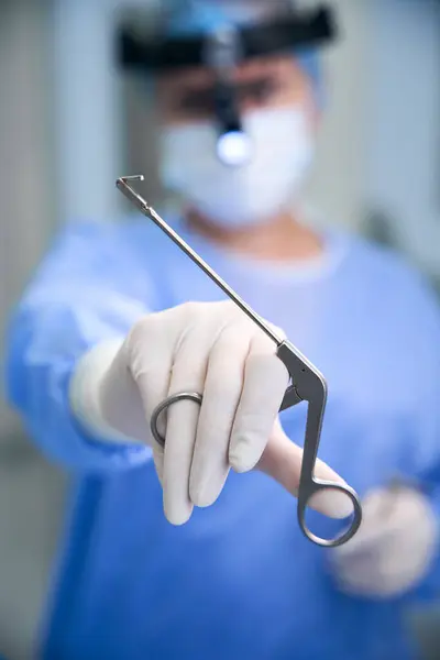 stock image Otolaryngologist surgeon holds special instrument made of medical steel in his hand, woman has a surgical headlamp on her head