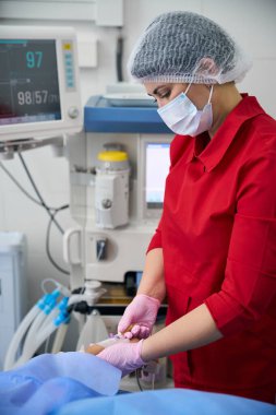 Experienced operating room nurse prepares a patient for surgery, she injects a drug into her vein clipart