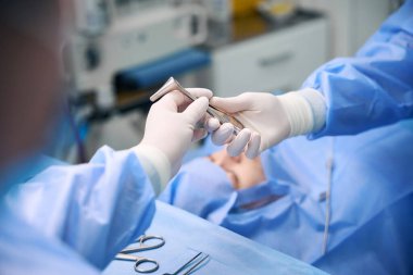 Deneyimli bir hemşire, özel aletler kullanarak bir doktora ameliyat sırasında yardımcı olur.