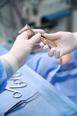 Experienced operating nurse hands the doctor a special instrument, hands in surgical gloves clipart