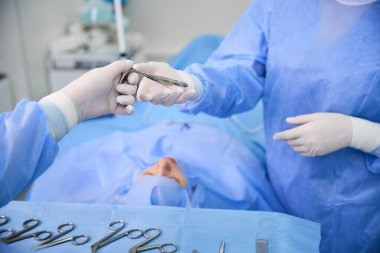 Cerrahi hemşiresi bir doktora metal bir alet verdi. Elleri ameliyat eldivenlerindeydi.