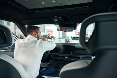 Beyaz tişörtlü yetişkin bir adamın araba kuaföründe yeni arabasında oturması. Yeni araba sahibi kavramı