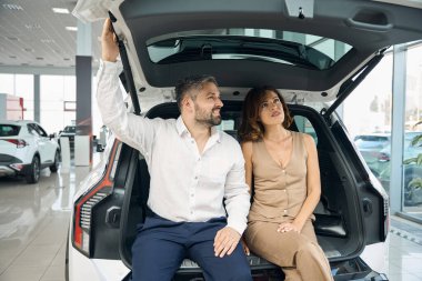 Genç adam ve kadın araba galerisinde yeni bir araba seçip satın alıyorlar.
