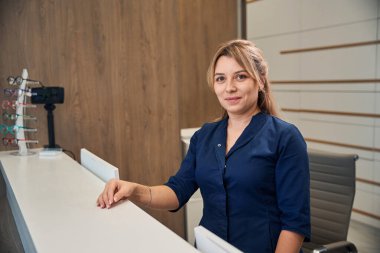 Profesyonel resepsiyonist, gelen ziyaretçilere yardım teklifinde bulunmak için masanın başında dikiliyor.