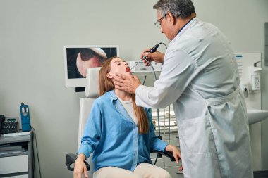 Tıbbi uzman, tedavi koltuğunda oturan bir hastaya burun ameliyatı yapıyor.